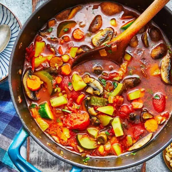 homemade vegetable soup in a dutch oven with a wooden spoon next to a bowl with two silver spoons.