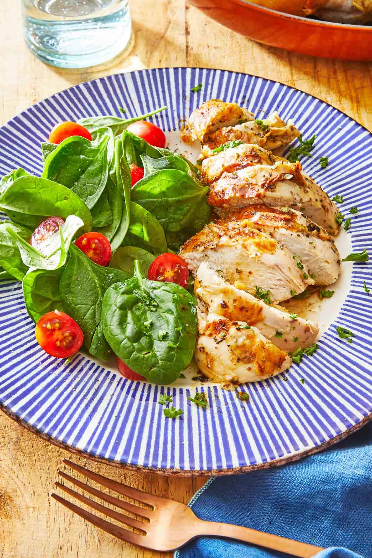 a piece of chicken sliced up on a plate with a spinach salad and cherry tomatoes.