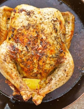 close up of a whole cooked chicken rubbed in italian seasoning in a skillet.