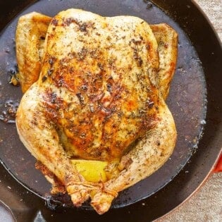 close up of a whole cooked chicken rubbed in italian seasoning in a skillet.