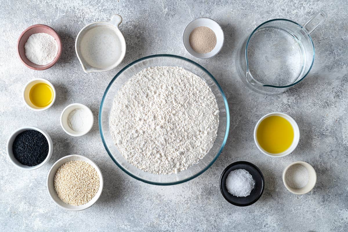 ingredients for barbari bread including water, yeast, sugar, flour, salt, olive oil, baking powder and nigella and sesame seeds.