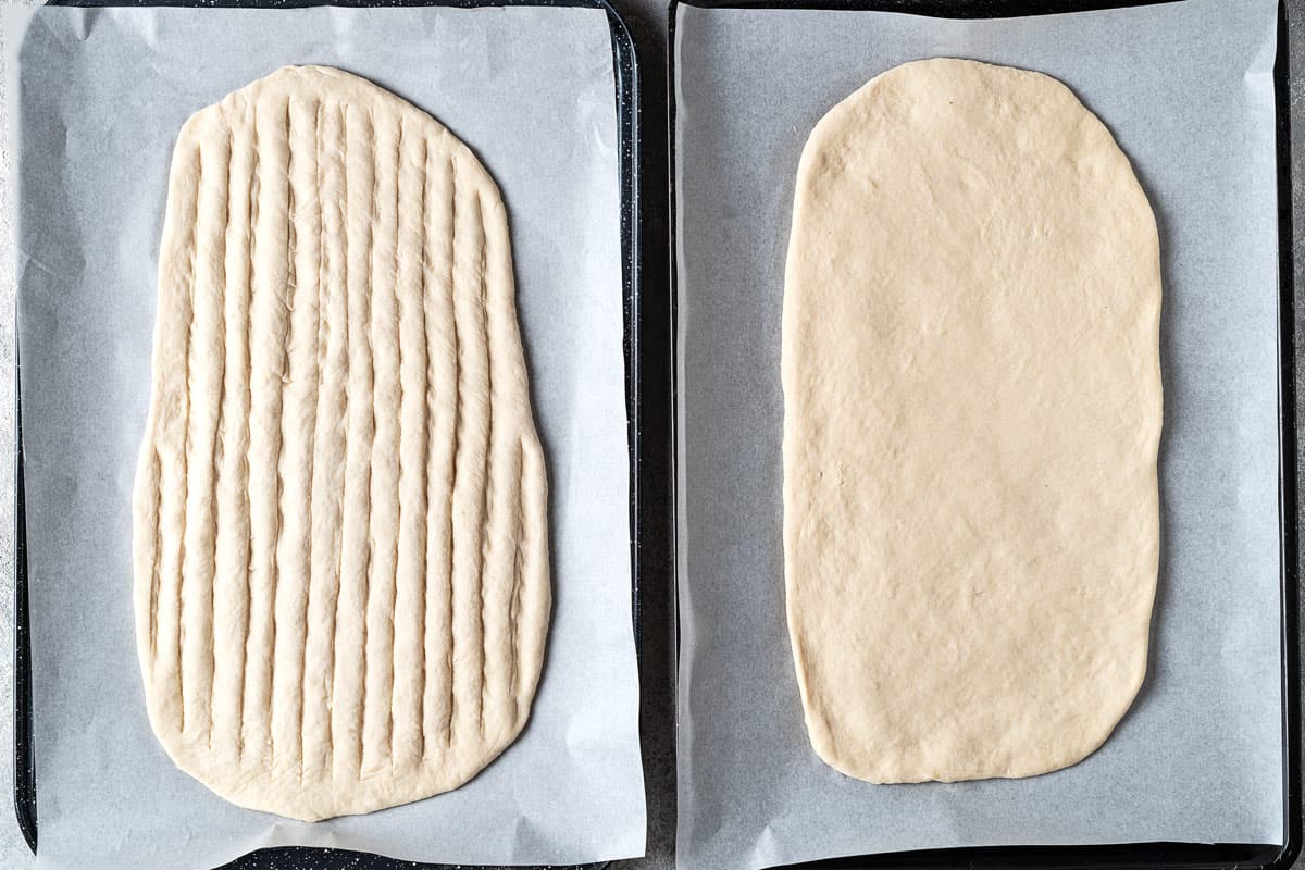 two pieces of unbaked barbari bread shaped on parchment lined baking sheets.