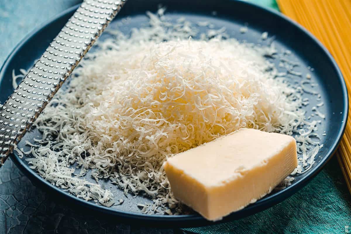 Fromage Pecorino Romano finement râpé à côté d'une râpe à fromage sur une assiette.