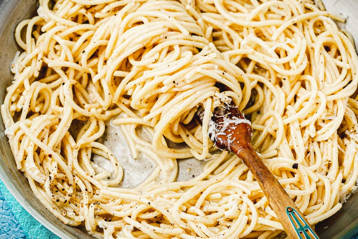 cacio e pepe being stirred with a wooden spoon in a skillet.