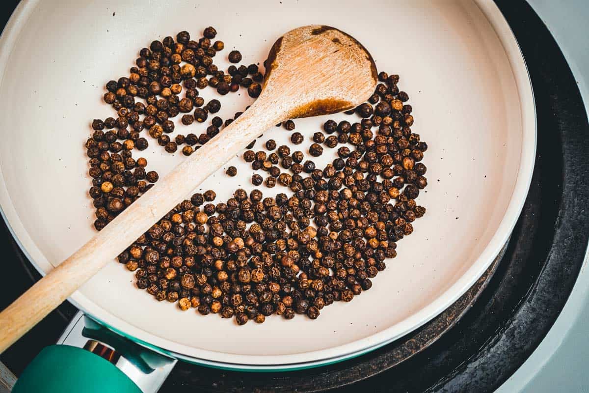 whole peppercorns being toasted in a skillet.