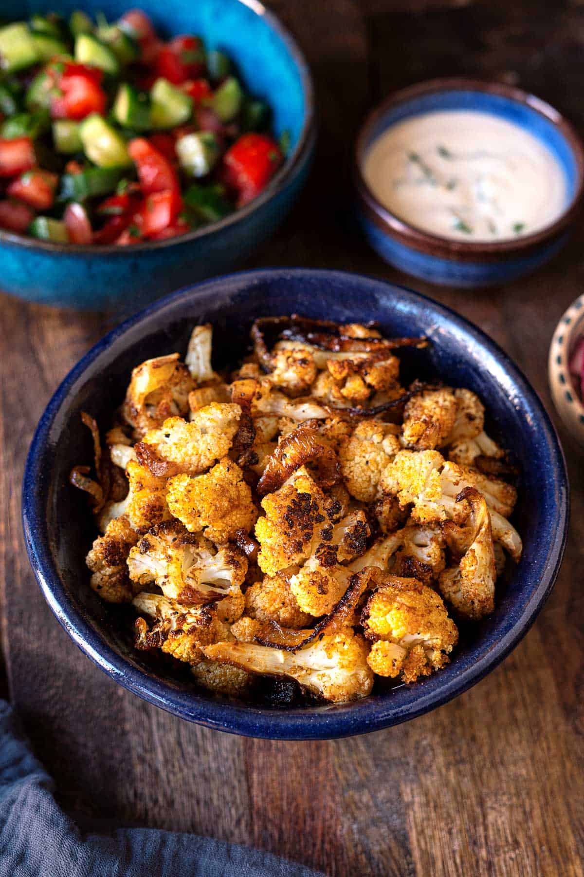 roasted cauliflower shawarma in a bowl with a sides of tahini sauce and salad.