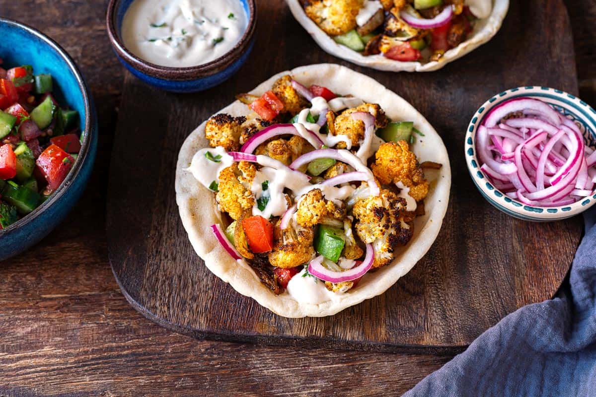 one cauliflower shawarma pita with a sides of tahini sauce, red onion and salad.