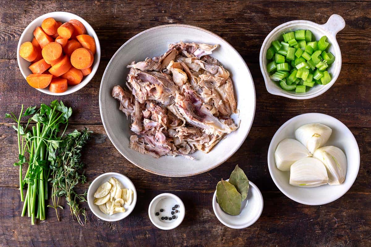 ingredients to chicken stock including carrots, celery, parsley stems, onion, thyme, bay leaves, peppercorn and chicken.