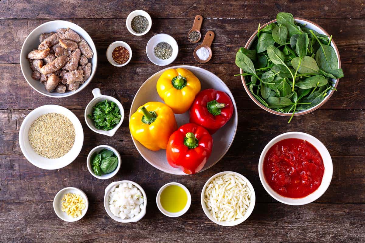 ingredients for italian stuffed peppers including bell peppers, fine bulgur wheat, olive oil, diced yellow onion, minced garlic, italian turkey sausage, spices, diced tomatoes, baby spinach, parsley, basil, and shredded mozzarella cheese.