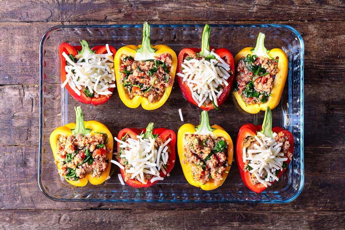 four red pepper and four yellow pepper halves stuffed with a meat filling in a baking dish.