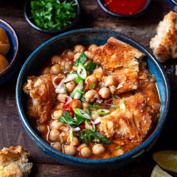 lablabi tunisian chickpea stew in a bowl, next to bowls of various toppings.