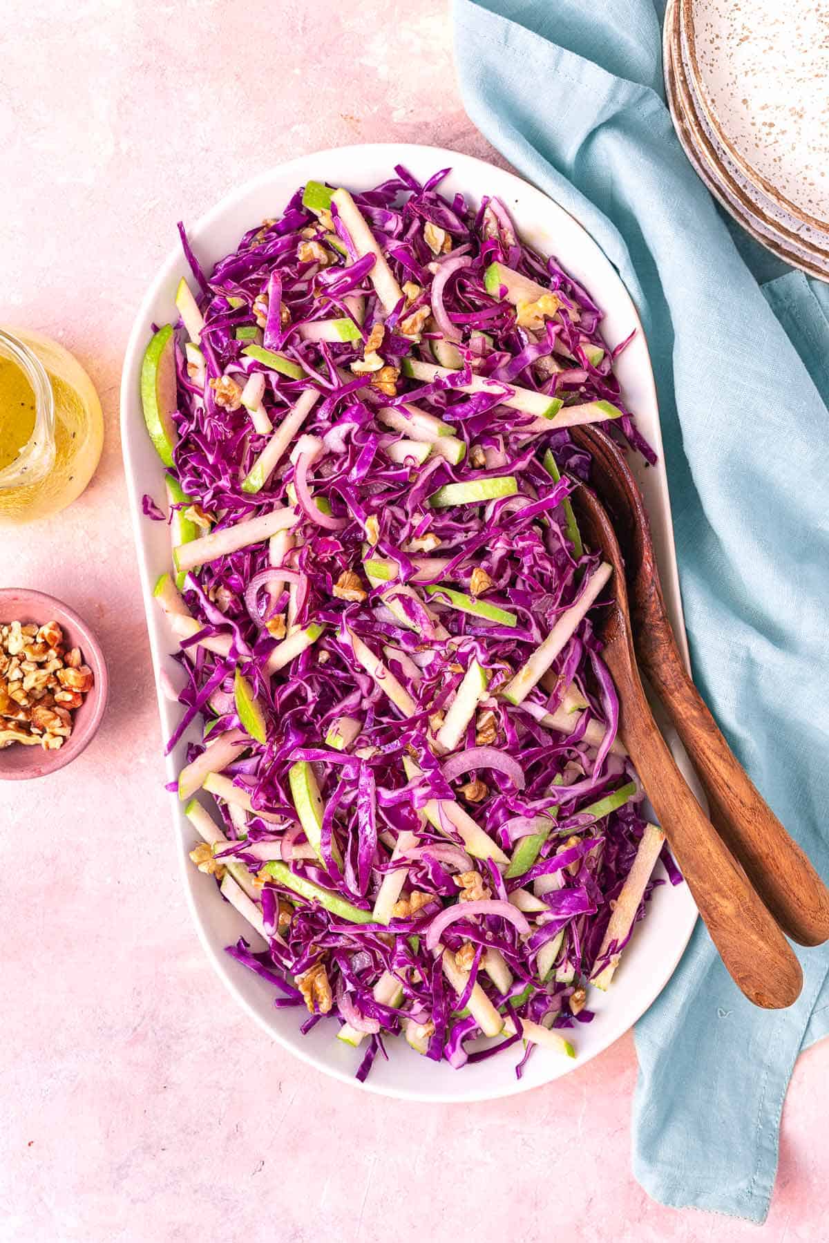 red cabbage salad in a large serving bowl with wooden serving utensils.