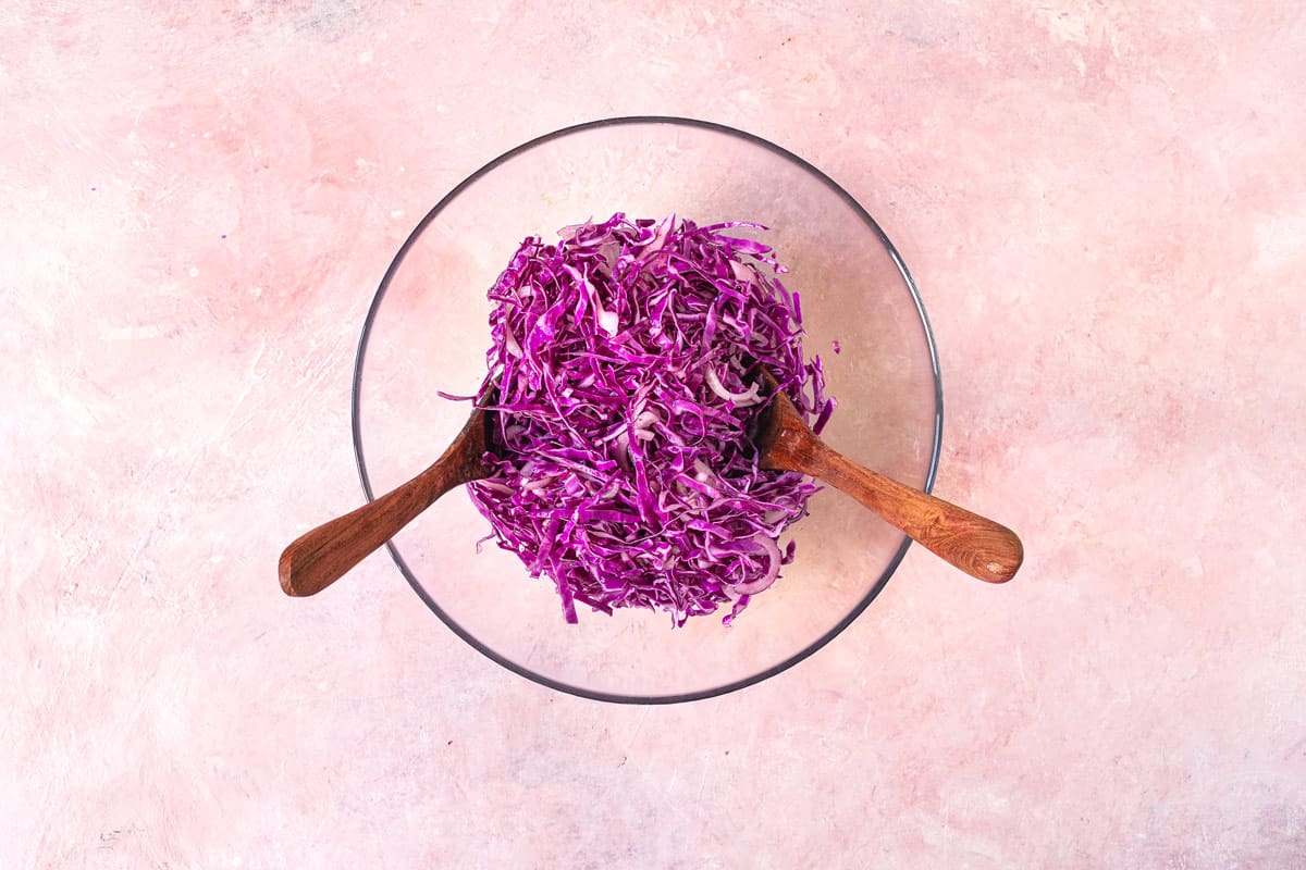 shredded red cabbage in a bowl with a wooden spoon and wooden fork.