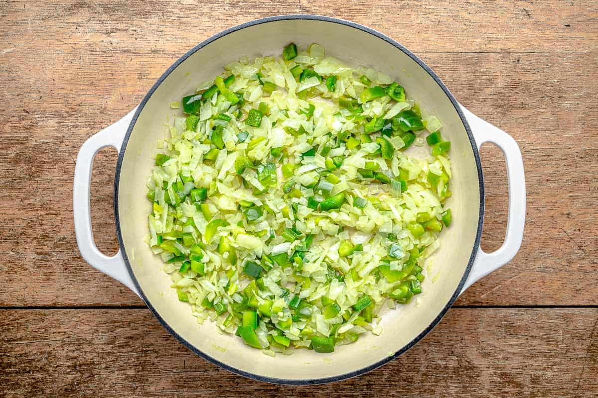 chopped yellow onions and green peppers being sauteed in a pot.