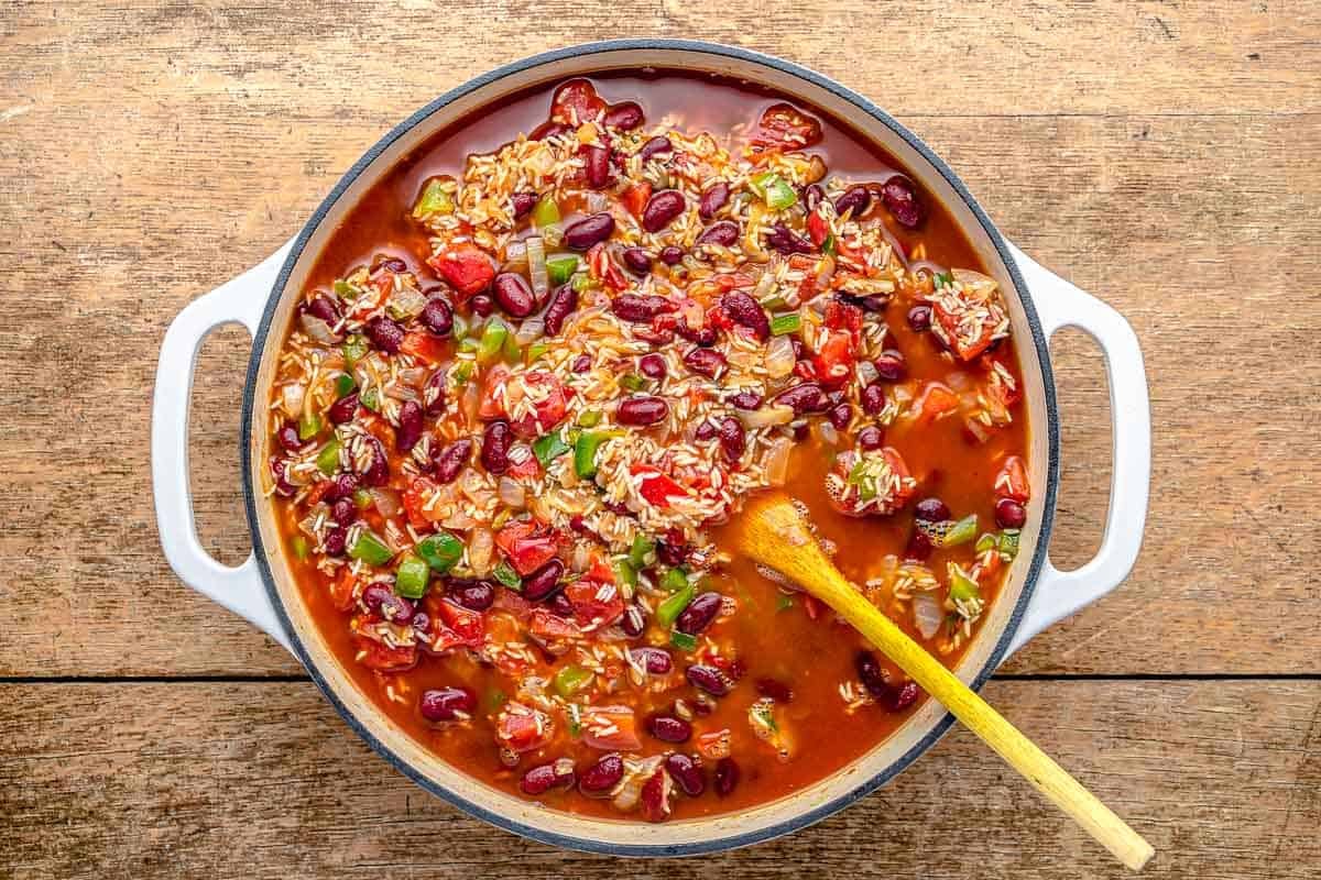 spanish rice and beans ingredients simmering in a pot with a wooden spoon.