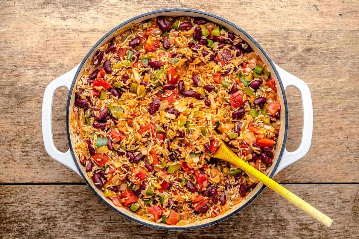 spanish rice and beans ingredients simmering in a pot with a wooden spoon.