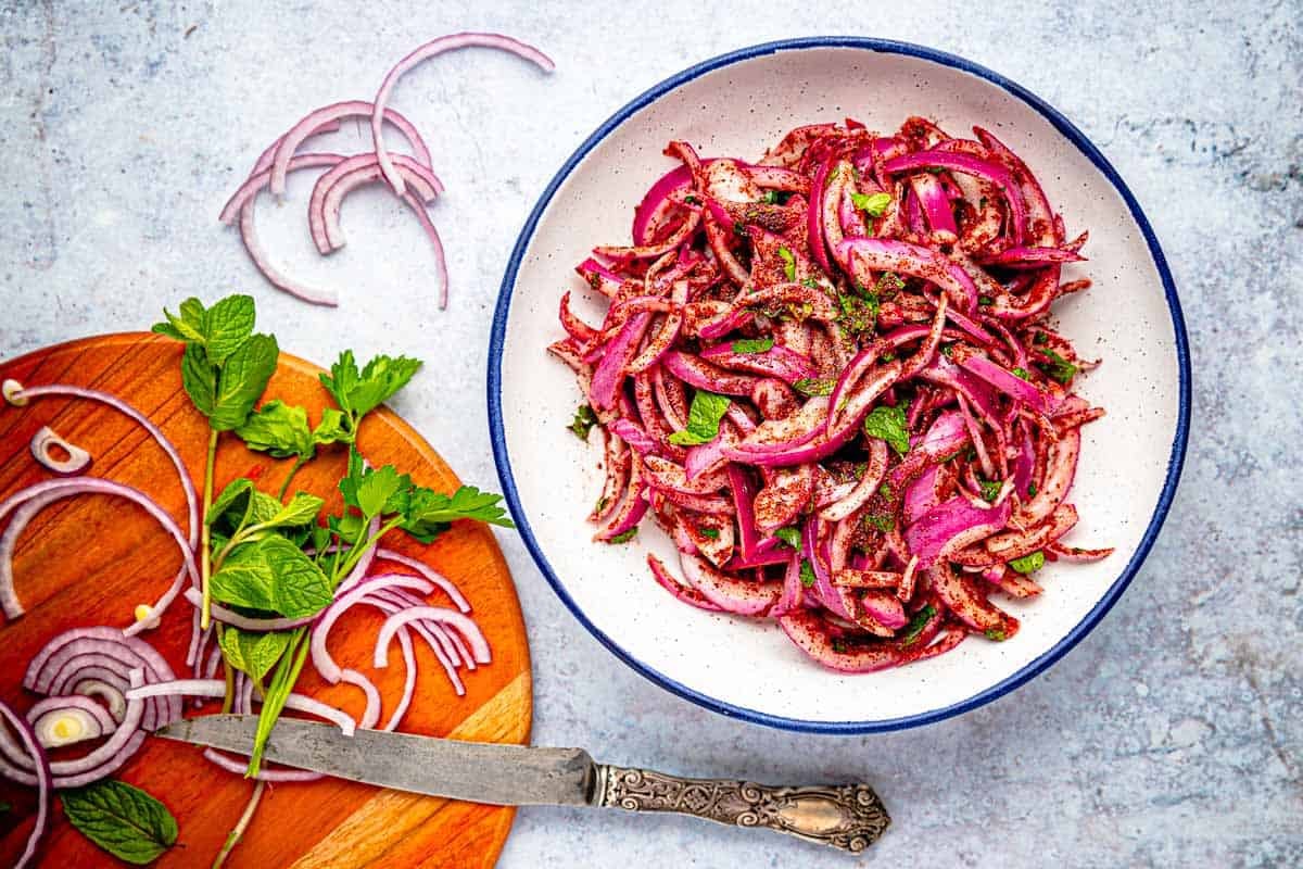 pickled red onions in a bowl next to a knife and cutting board holding leftover ingedients.