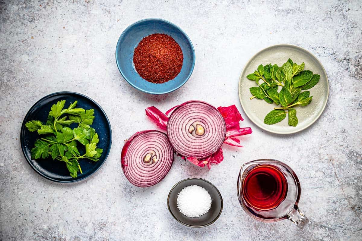 ingredients for pickled onions including red onion, red wine vinegar, sumac, salt, parsley and mint.