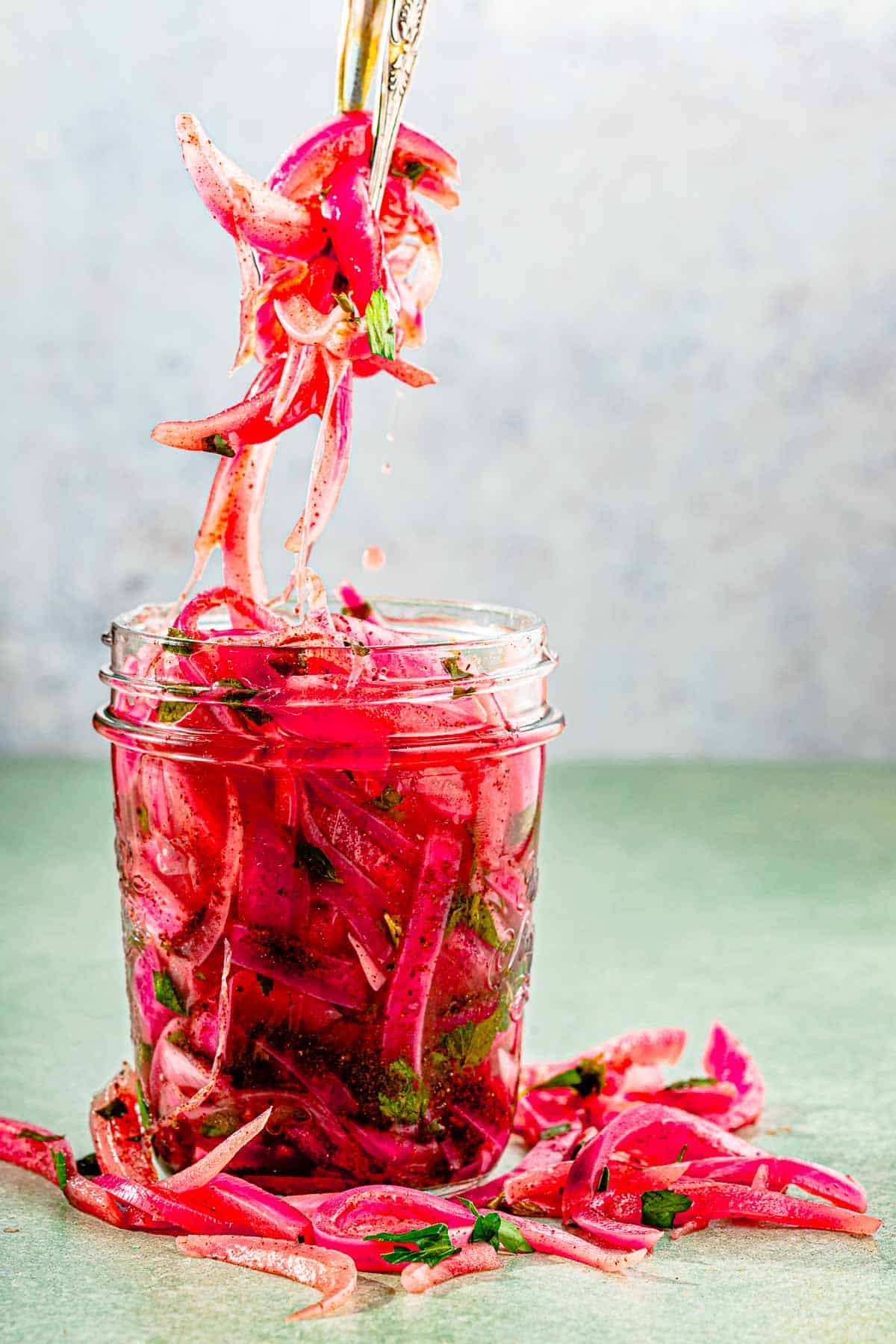 pickled onions being removed from a jar with tongs.