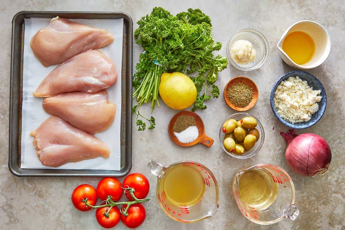 ingredients for mediterranean chicken including chicken breasts, parsley, lemon, salt, pepper, garlic, oregano, olive oil, white wine, broth, red onion, tomatoes, olives and feta cheese.