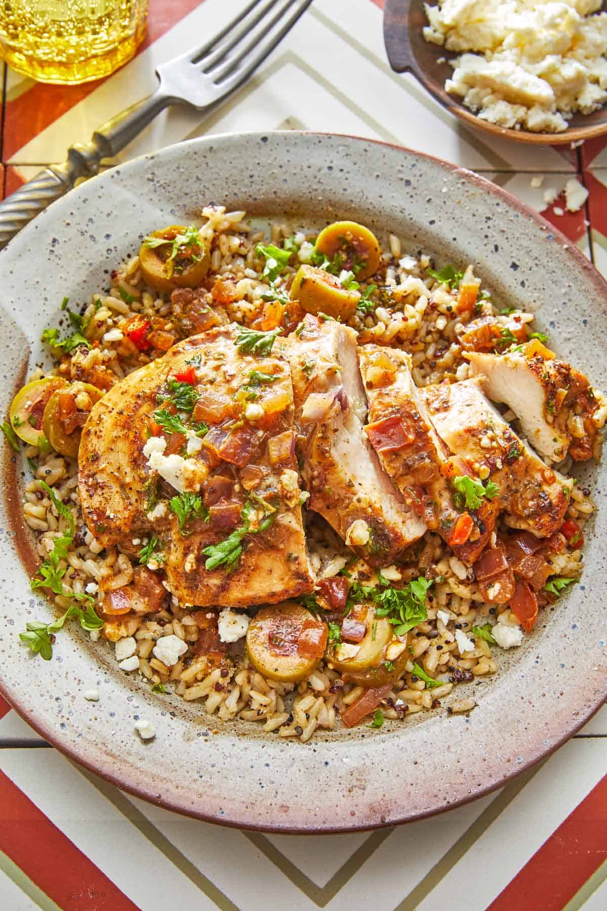 sliced mediterranean chicken with tomatoes and olives on a bed of orzo on a plate.