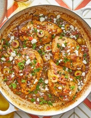 4 pieces of mediterranean chicken with tomatoes and olives topped with feta in a large pot.