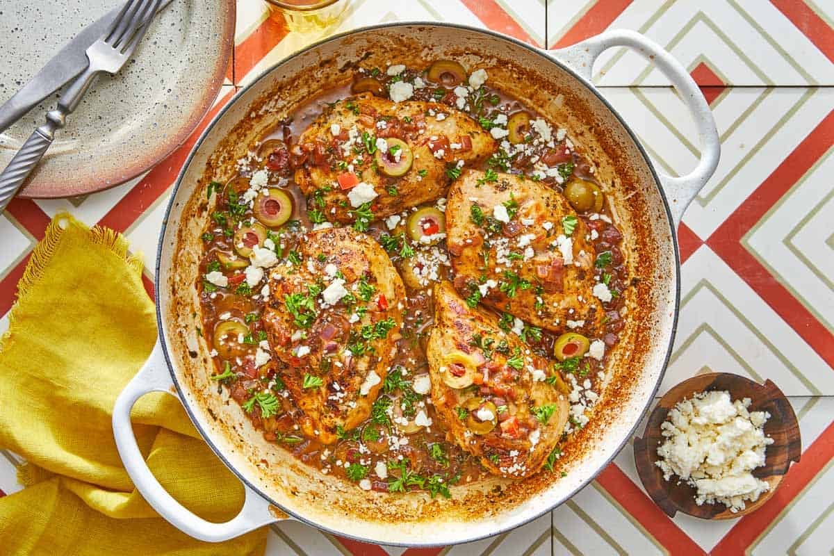 4 pieces of mediterranean chicken with tomatoes and olives topped with feta in a large pot.
