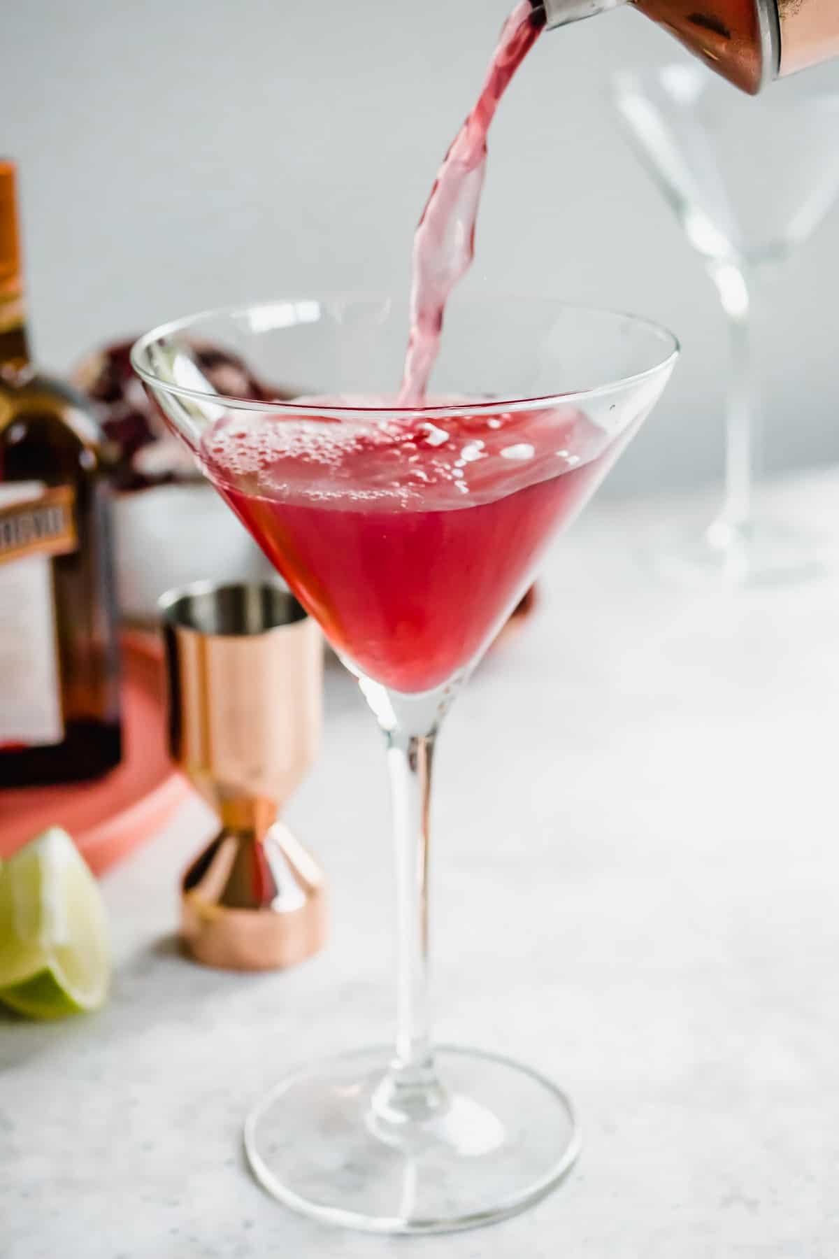 a pomegranate martini being poured from a martini shaker into a tall martini glass.