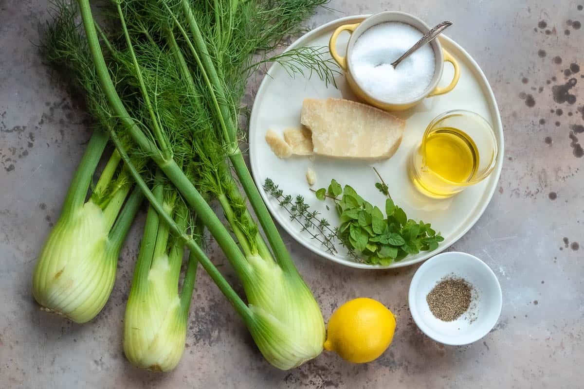 ingredients for roasted fennel with parmigiano cheese including 3 fennel bulbs, olive oil, oregano, thyme, fennel fronds, lemon, sea salt, pepper, and parmigiano-reggiano cheese.