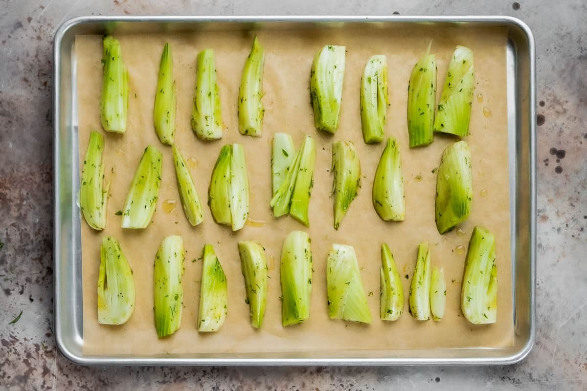 pieces of seasoned uncooked fennel on a baking sheet lined with parchment paper.