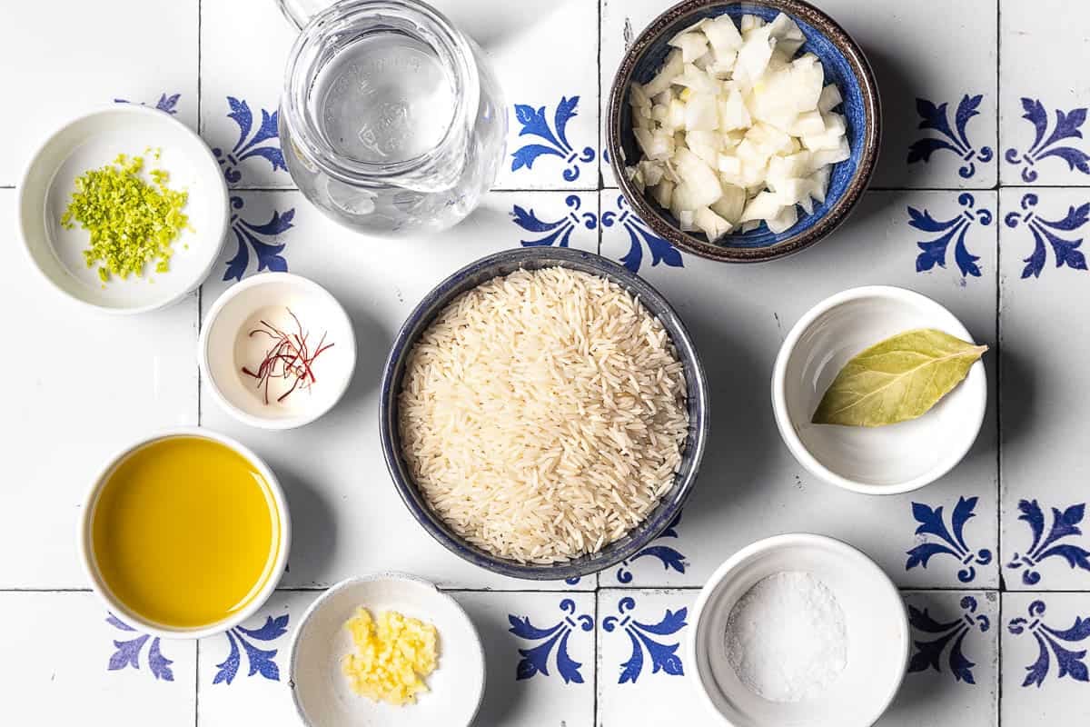 ingredients for saffron rice including saffron, basmati rice, olive oil, chopped onion, garlic, water, a bay leaf, lime zest, and salt.