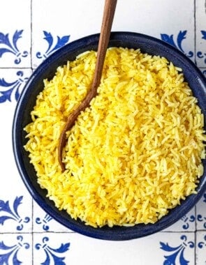 saffron rice in a bowl with a wooden spoon.