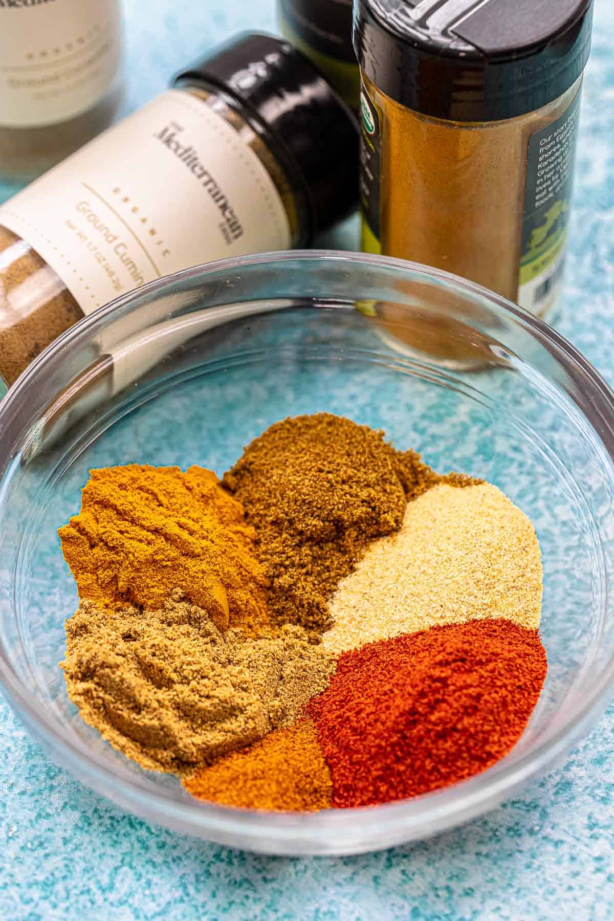 homemade shawarma spice blend including ground cumin, turmeric powder, ground coriander, garlic powder, sweet spanish paprika, ground cloves and cayenne pepper in a bowl next to a bottle of ground cumin and another spice.