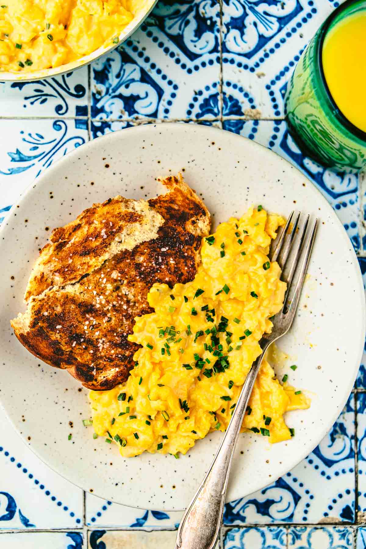 soft scrambled eggs topped with chives next to toast on a plate with a fork.