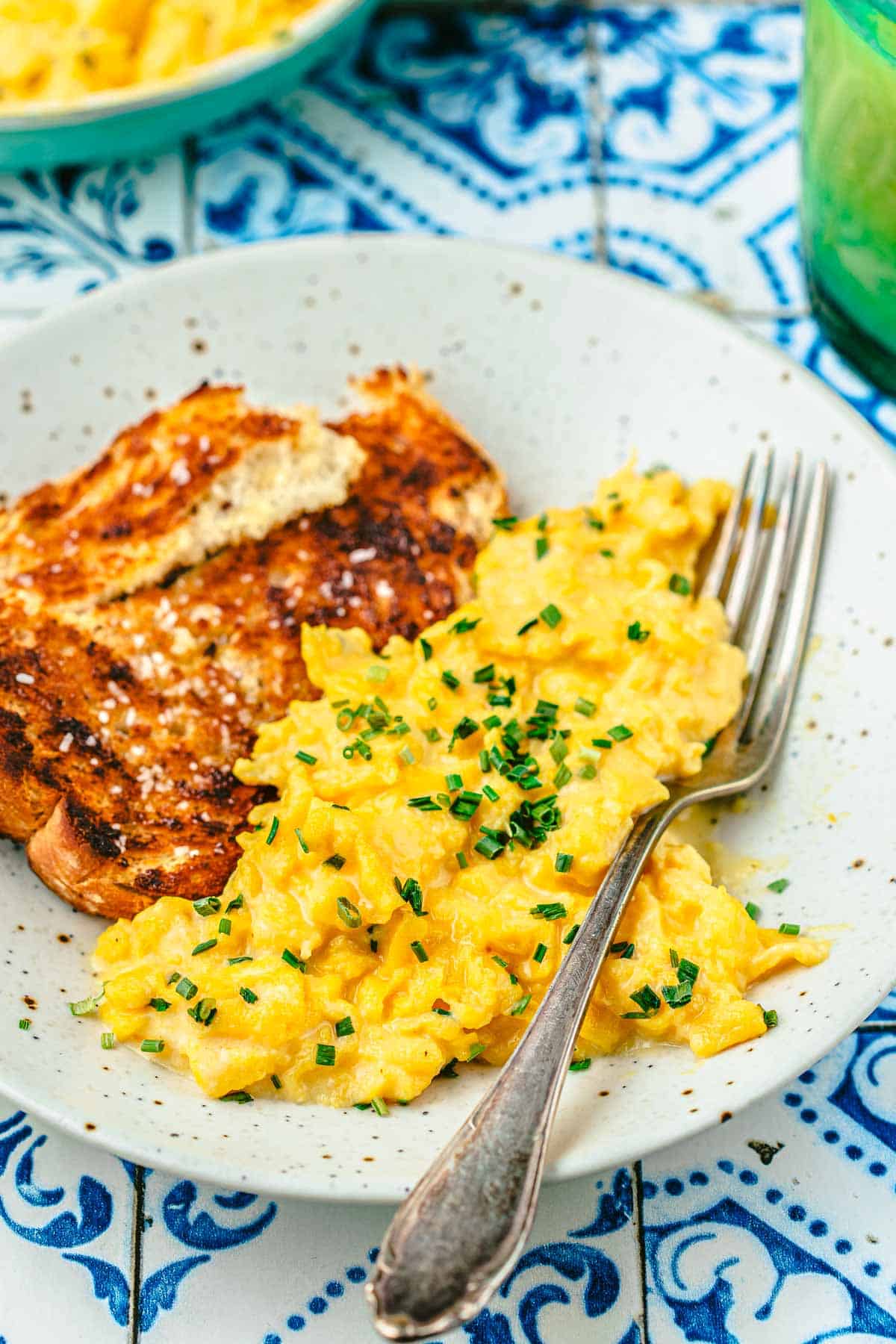 soft scrambled eggs topped with chives next to toast on a plate with a fork.