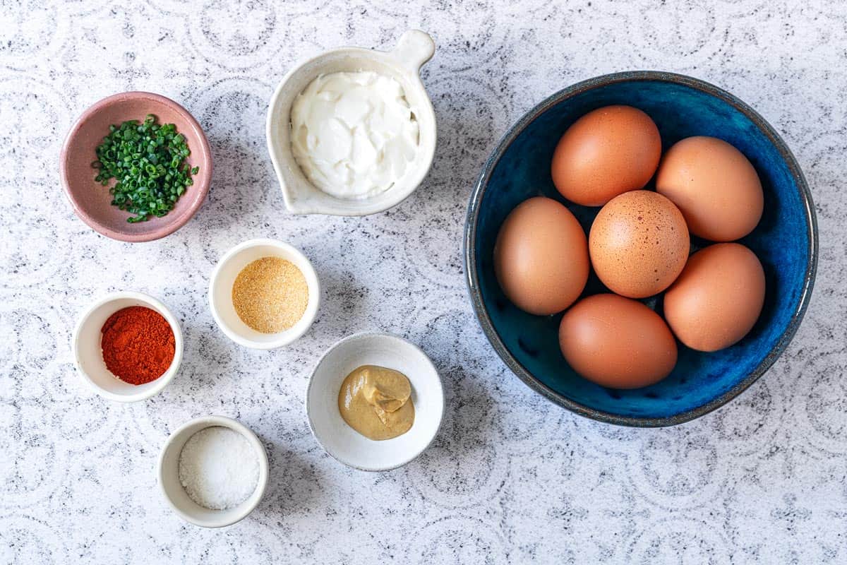 ingredients for deviled eggs including eggs, yogurt, chives, paprika, garlic powder, dijon mustard and kosher salt.