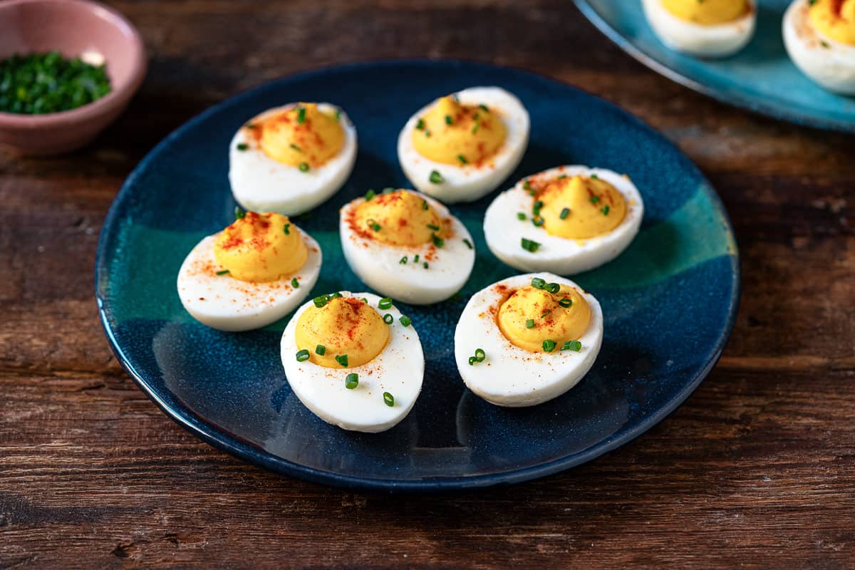 seven deviled eggs on a plate topped with paprika and chives.