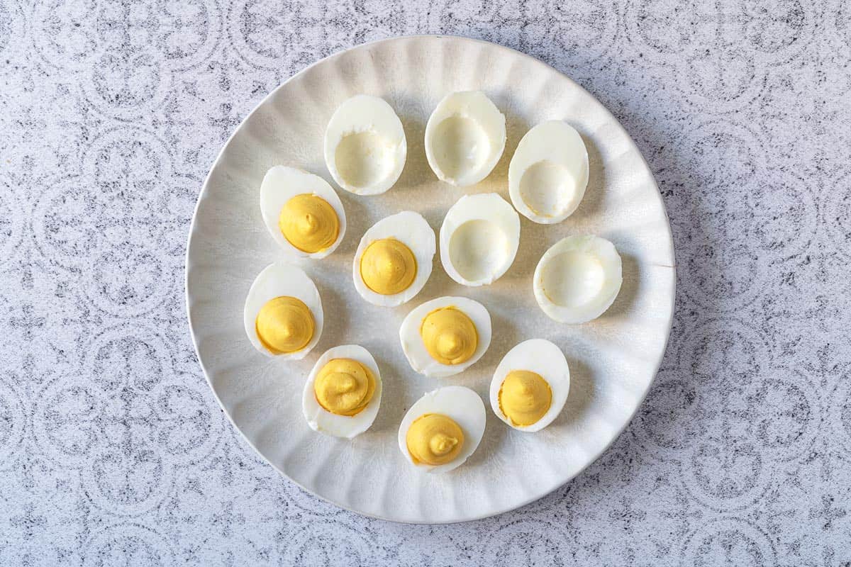 deviled egg filling being added to 12 hard boiled egg halves.