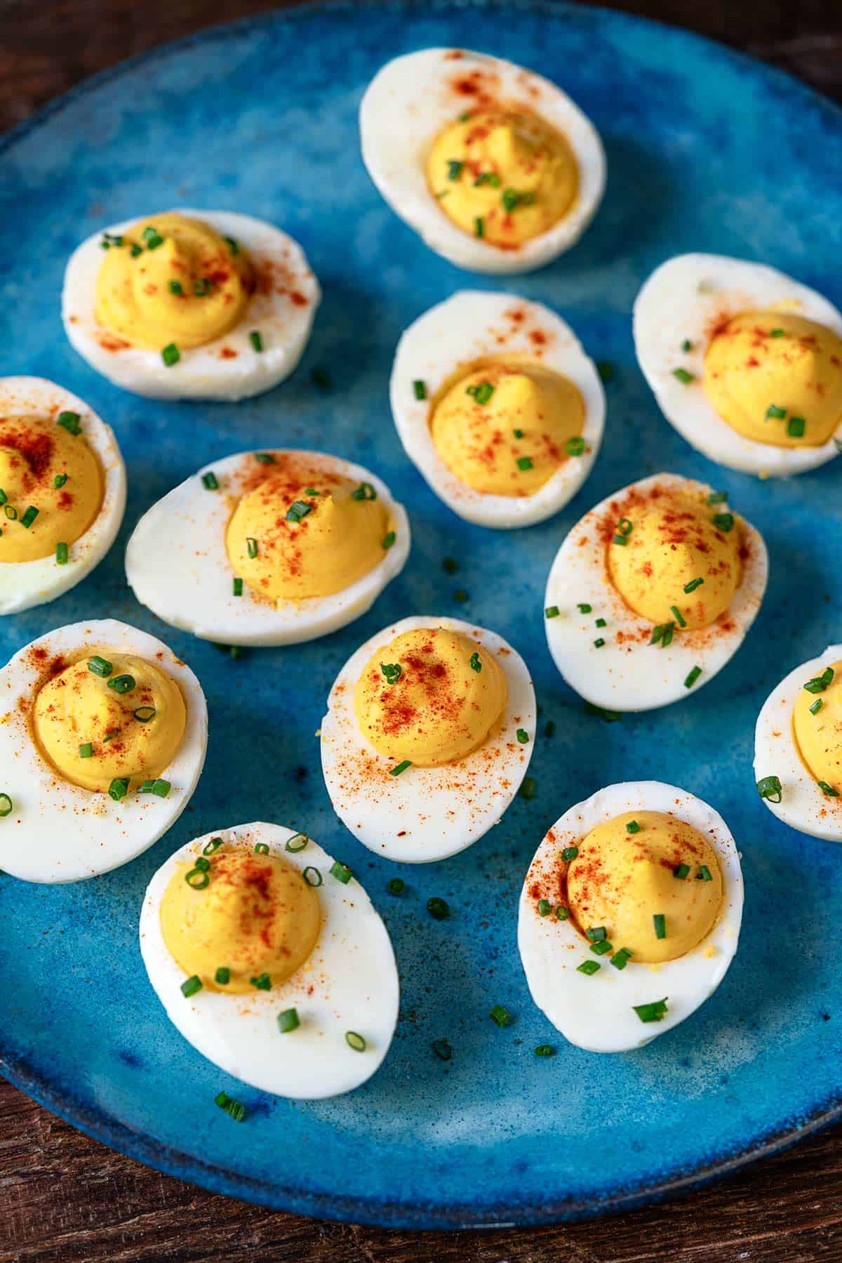 12 deviled eggs on a plate topped with paprika and chives.