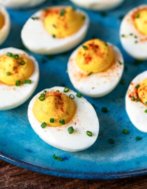 close up of 8 deviled eggs topped with paprika and chives on a plate .