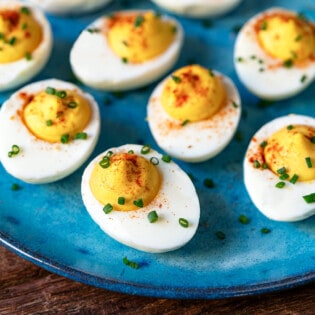 close up of 8 deviled eggs topped with paprika and chives on a plate .