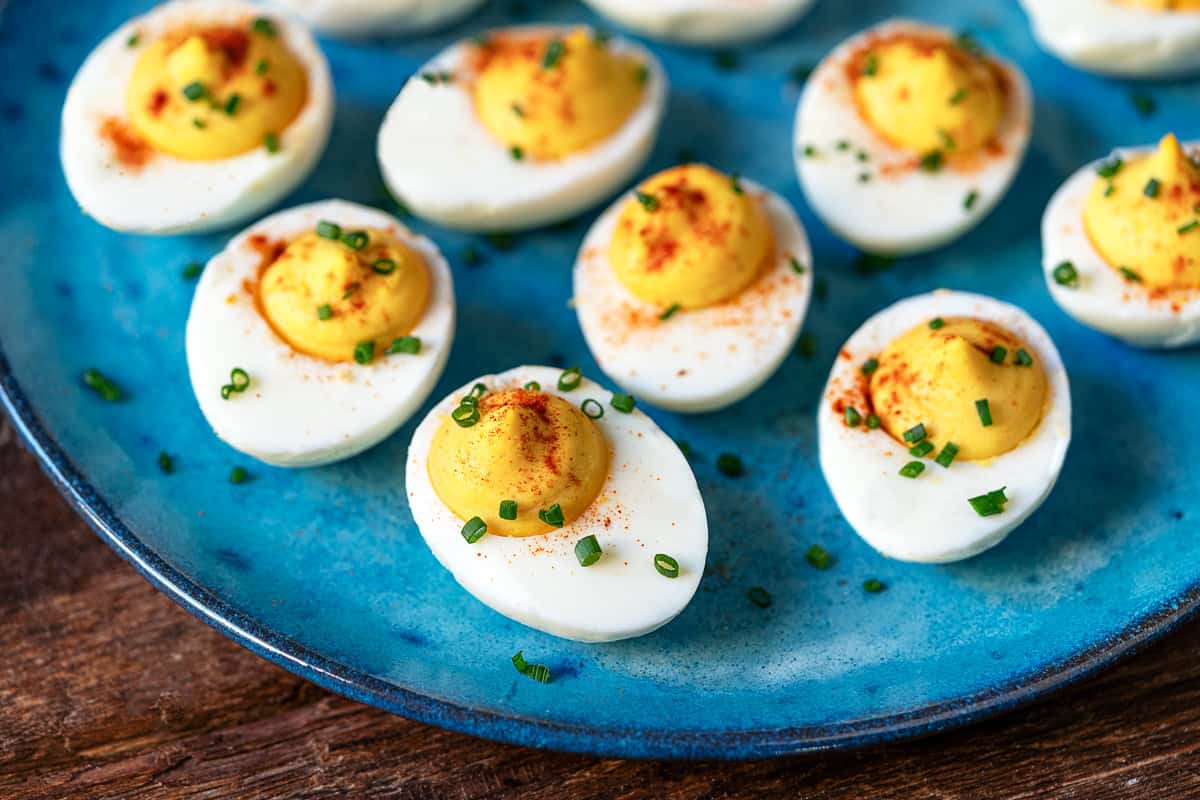 close up of 8 deviled eggs topped with paprika and chives on a plate .