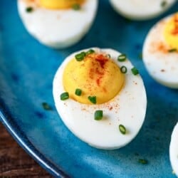 close up of a deviled egg topped with paprika and chives on a plate.