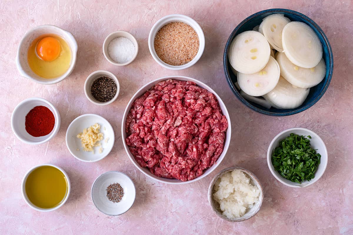 ingredients for lamb meatballs with caramelized onions including olive oil, onions, spices, ground lamb, breadcrumbs, egg, garlic, and parsley.