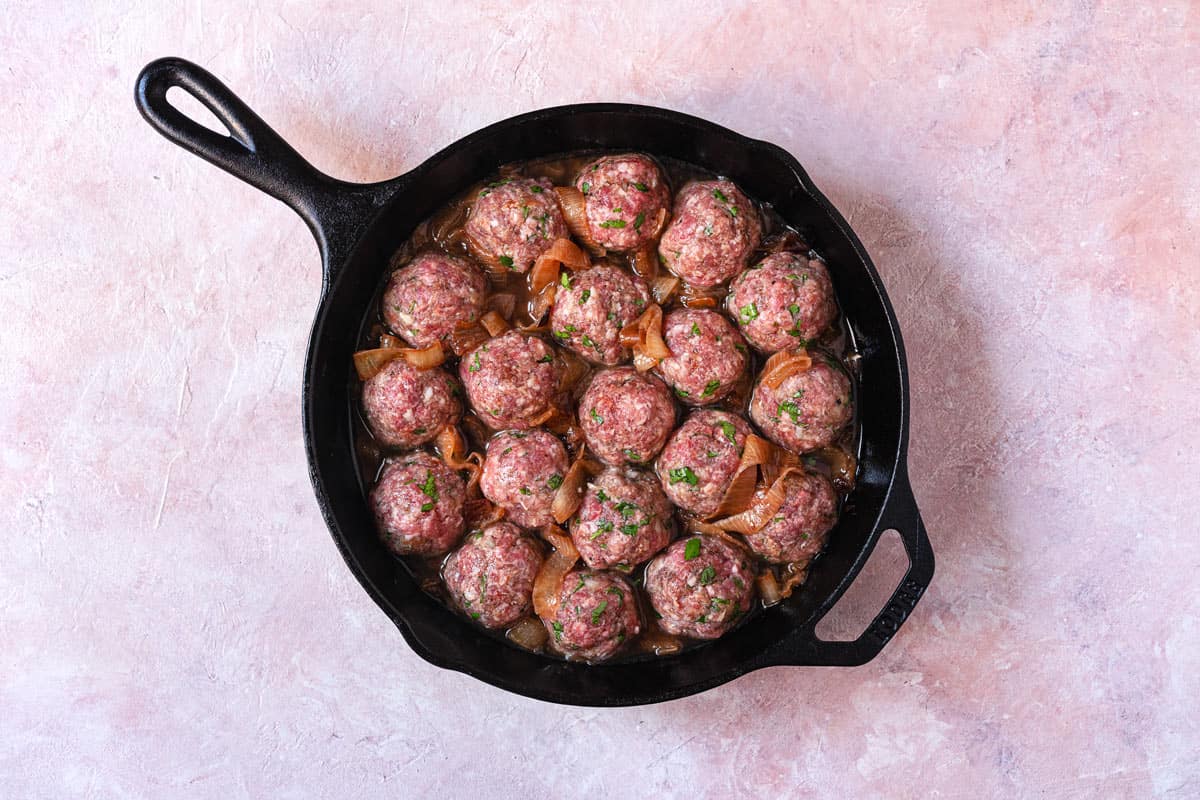 uncooked lamb meatballs in a cast iron skillet.