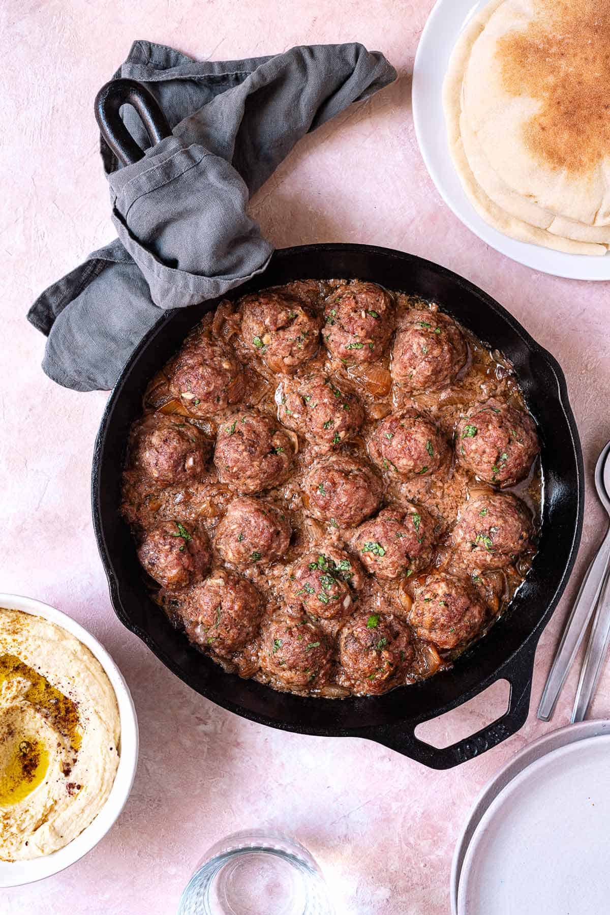 lamb meatballs in a cast iron skillet next to a side of hummus and pita bread.