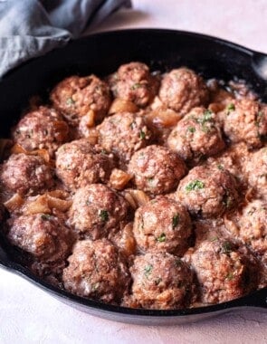cooked meatballs with caramelized onions in a cast iron skillet.