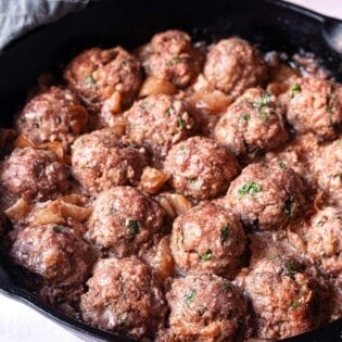 cooked meatballs with caramelized onions in a cast iron skillet.