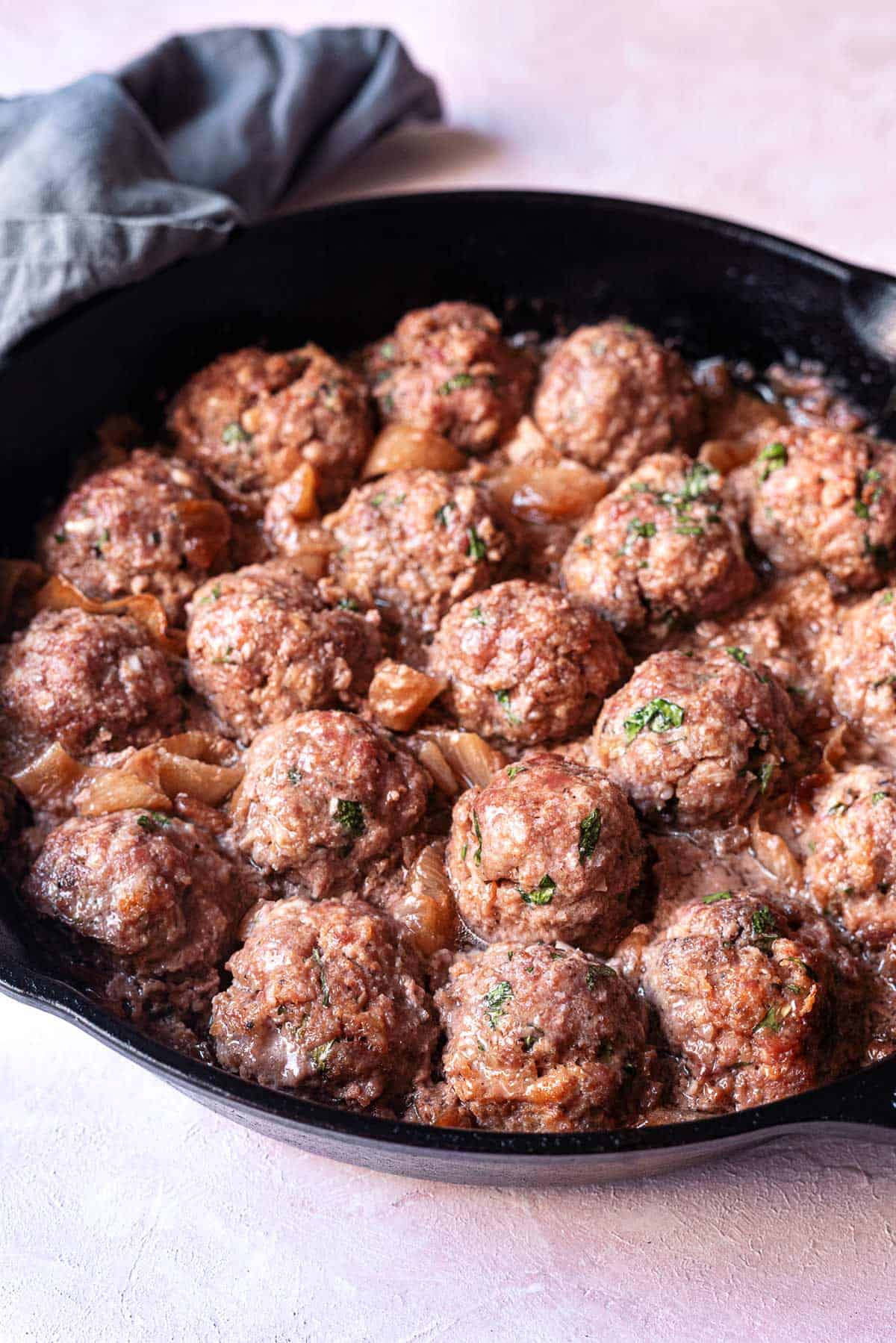 cooked meatballs with caramelized onions in a cast iron skillet.