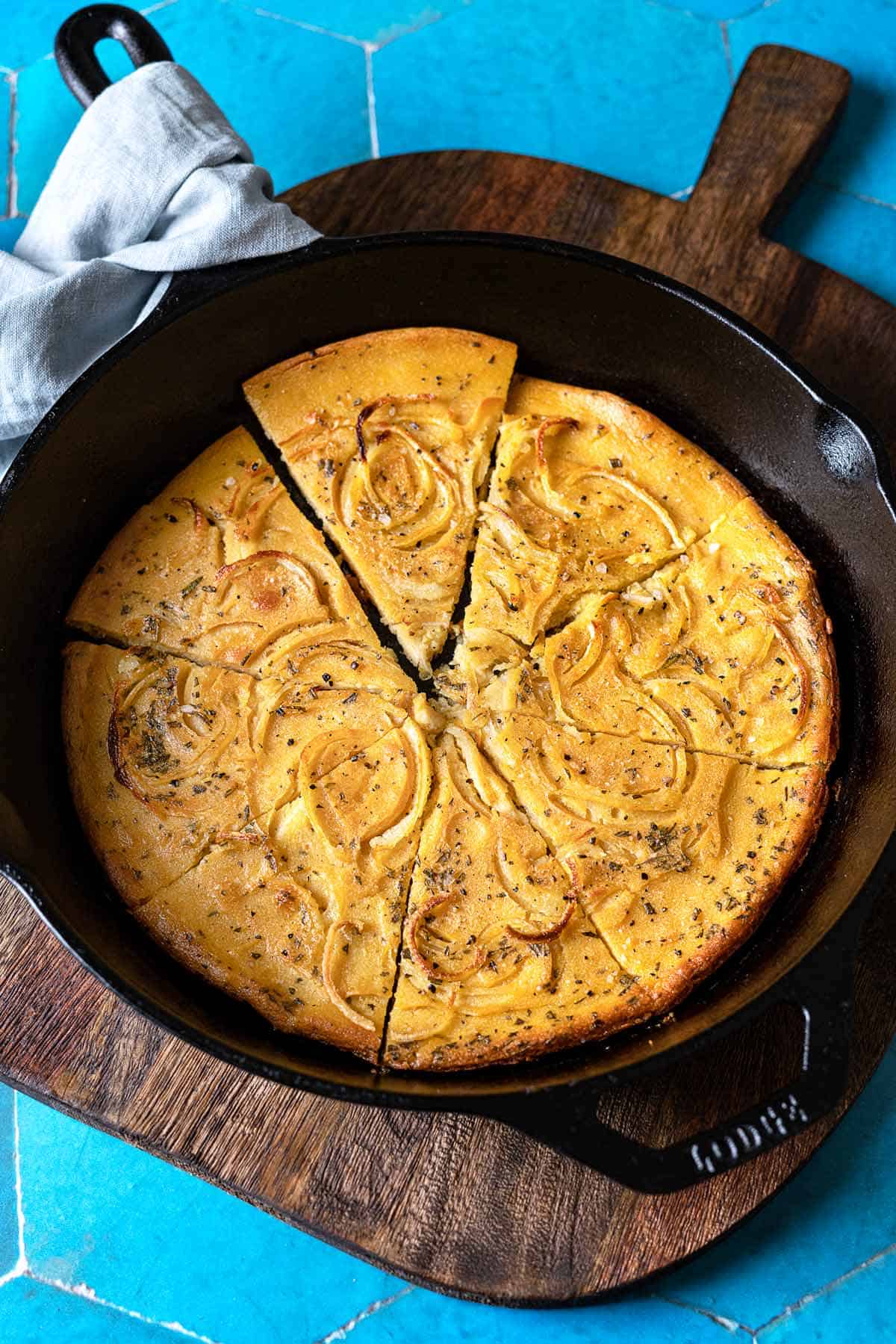 a baked farinata italian chickpea pancake sliced into pieces in a cast iron skillet.